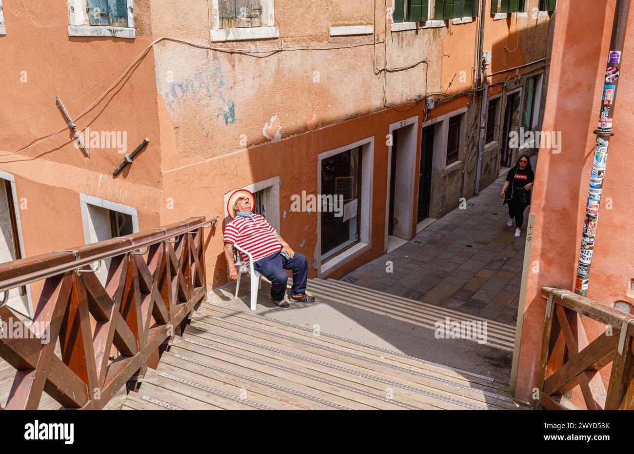 Ein Gondoliere in einem traditionellen rot-weißen Hemd sitzt in einem Stuhl, der von Ponte Vinanti in Dorsoduro und Santa Croce, Venedig, Italien, schläft Stockfoto