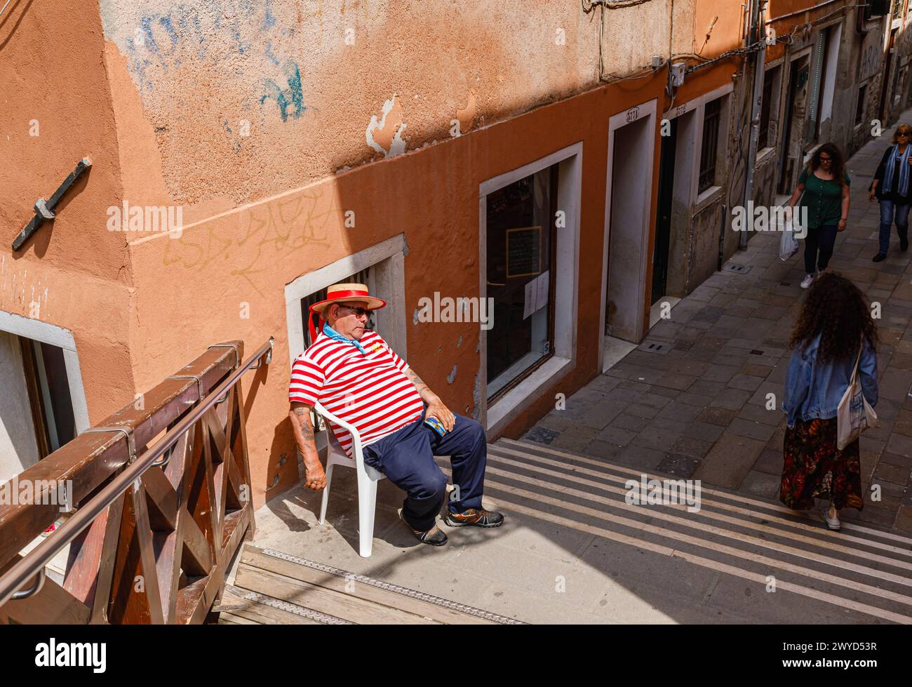 Ein Gondoliere in einem traditionellen rot-weißen Hemd sitzt in einem Stuhl, der von Ponte Vinanti in Dorsoduro und Santa Croce, Venedig, Italien, schläft Stockfoto