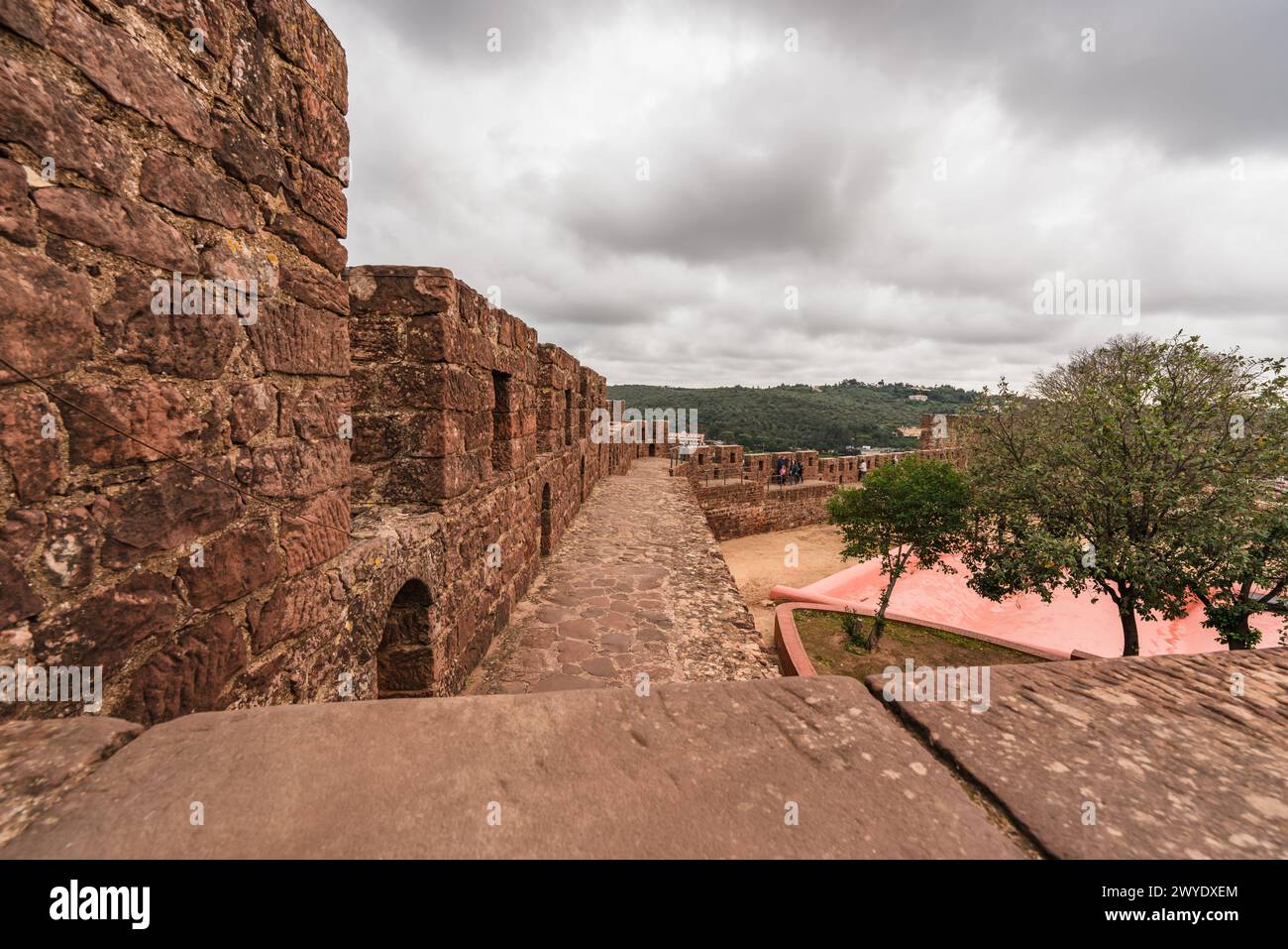 Innerhalb der mächtigen roten Mauern von Silves Castle betrachtet ein Besucher die riesige Geschichte, die sich vor ihm erstreckt Stockfoto