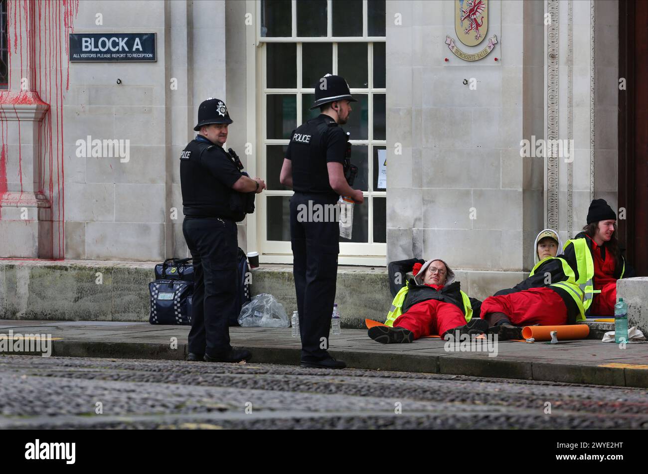 Ein Polizist interagiert mit Demonstranten, die den Eingang zur County Hall während der Demonstration blockieren. Unterstützer der Palästinensischen Aktion blockieren den Eingang zur County Hall mit Sperren und sprühen rote Farbe auf das Äußere des Gebäudes. Die Demonstranten fordern, dass der Stadtrat von Somerset den Mietvertrag für Büroflächen beendet, die sie an Elbit Systems in Aztec West, Bristol, vermieteten. Sie argumentieren, dass die von Elbit Systems in Großbritannien hergestellten Waffen von der israelischen Verteidigungsstreitkräfte gegen Palästinenser in Gaza und anderswo eingesetzt werden. Bei den israelischen Bombenanschlägen im Gazastreifen sind über 30.000 Palästinenser ums Leben gekommen Stockfoto