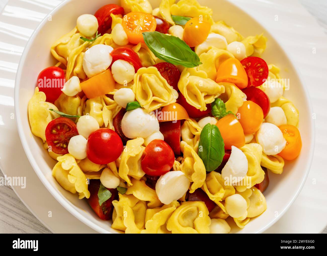 Tortellini-Salat mit Kirschtomaten, Mini-Mozzarella, frischen Basilikumblättern in weißer Schüssel, niederländischer Blickwinkel, Nahaufnahme Stockfoto