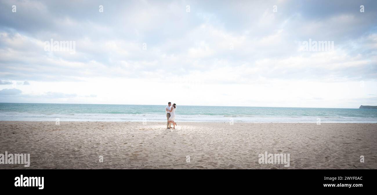 Ein Paar, das an einem ruhigen Strand teilnimmt: Ein Moment der Liebe und Verbindung auf unberührtem Sand unter einem riesigen Himmel Stockfoto