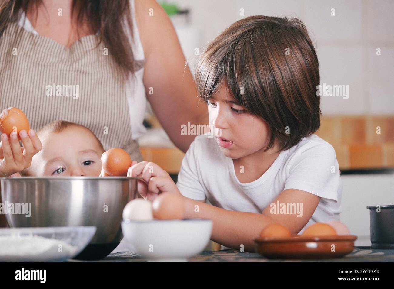 Kinder brechen Eier und legen sie in eine Schüssel während der Zubereitung eines Kuchens mit ihrer Mutter in der Küche zu Hause. Stockfoto