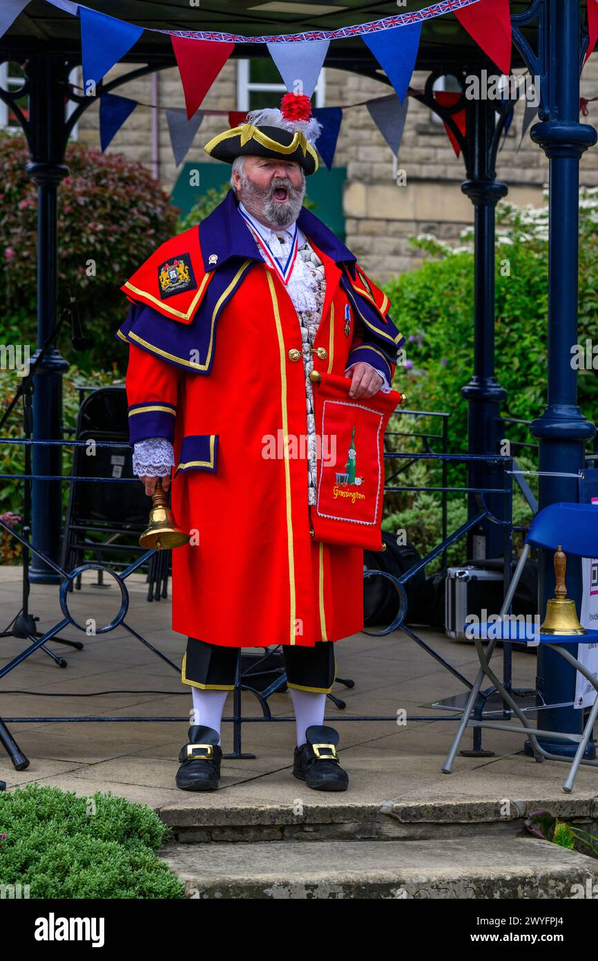 Männlicher Stadtschrei (farbenfrohe rote Flechtbeschriftung) verkündet Ankündigung und macht laute öffentliche Proklamation - Ilkley, West Yorkshire England Großbritannien. Stockfoto