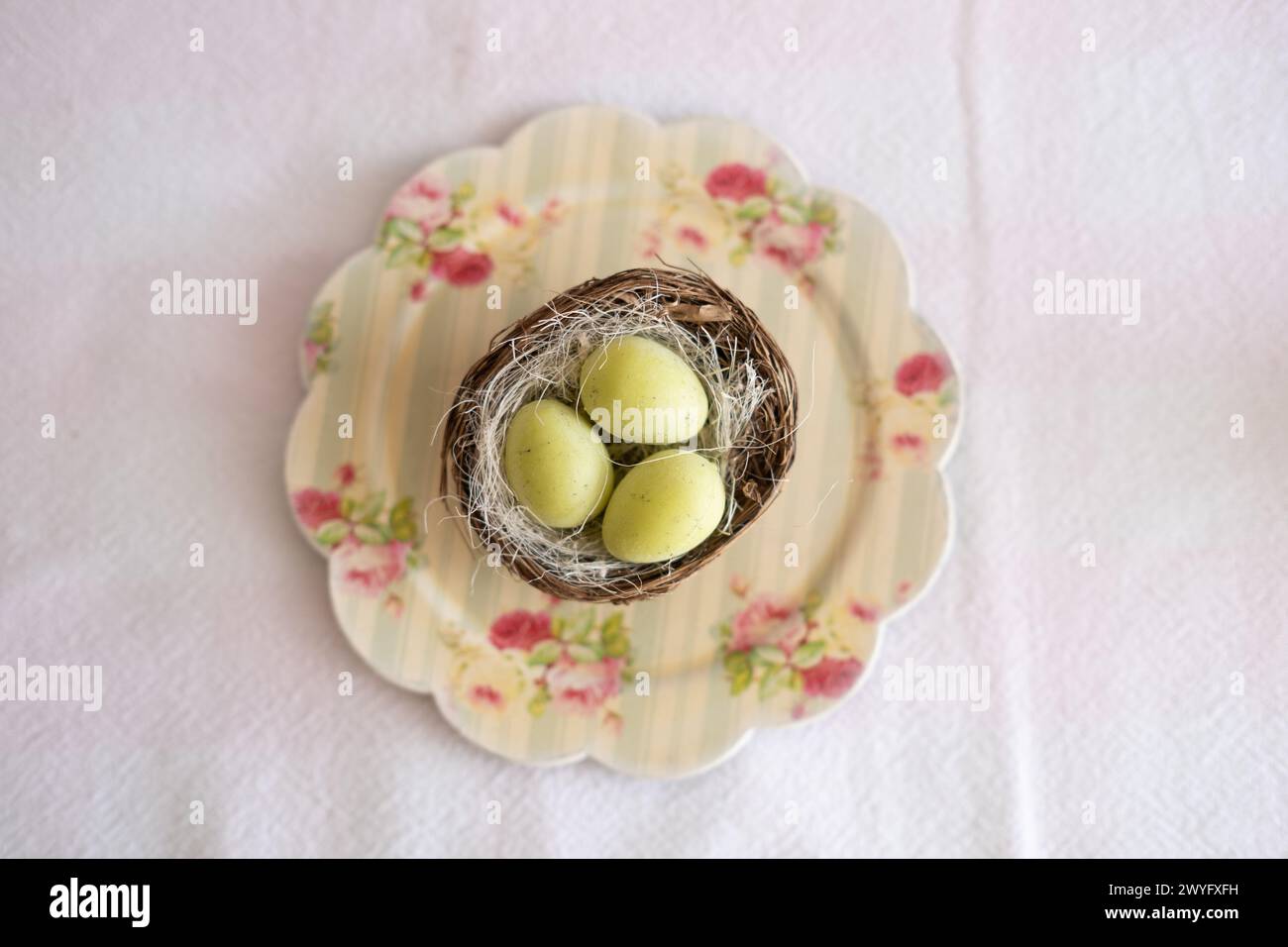 Blick von oben auf einen kleinen Teller mit einem kleinen Nest mit drei Ostereiern auf einem Osterbonbon-Tisch. Typische Osterbonbons auf einem festlichen Festtisch Stockfoto