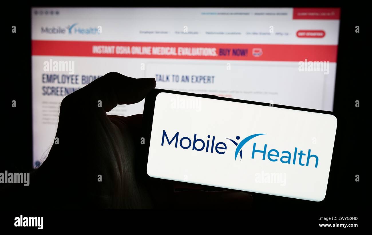 Person, die ein Mobiltelefon mit dem Logo der amerikanischen Firma Mobile Health Management Services Inc. Vor der Webseite hält. Schwerpunkt auf dem Display des Telefons. Stockfoto