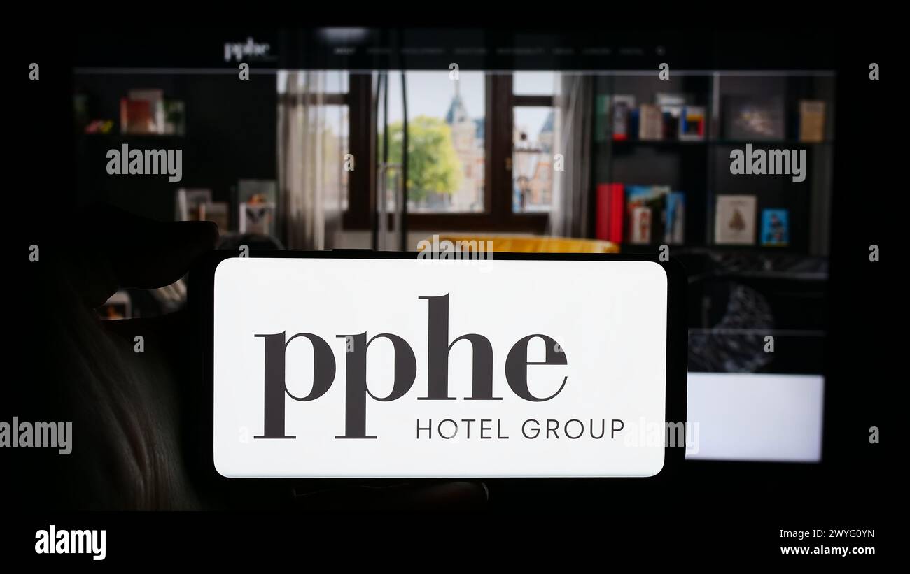 Person, die ein Handy mit dem Logo des britischen Hotelunternehmens PPHE Hotel Group Limited vor der Webseite hält. Schwerpunkt auf dem Display des Telefons. Stockfoto