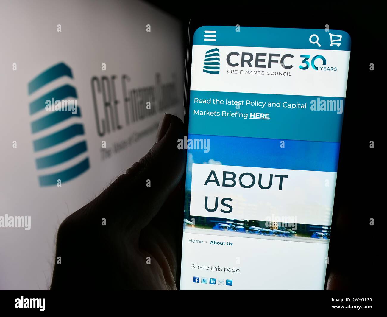 Person mit Mobiltelefon und Website des Wirtschaftsverbandes CRE Finance Council (CREFC) vor dem Logo. Konzentrieren Sie sich auf die Mitte des Telefondisplays. Stockfoto