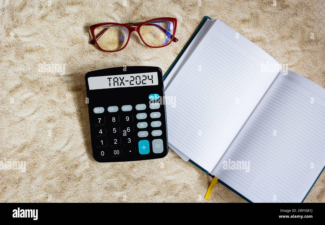 Das Wort Steuer 2024 auf einem Rechner. Unternehmenskonzept und Steuerkonzept. Taschenrechner, Buch, Brille auf dem Tisch. Stockfoto
