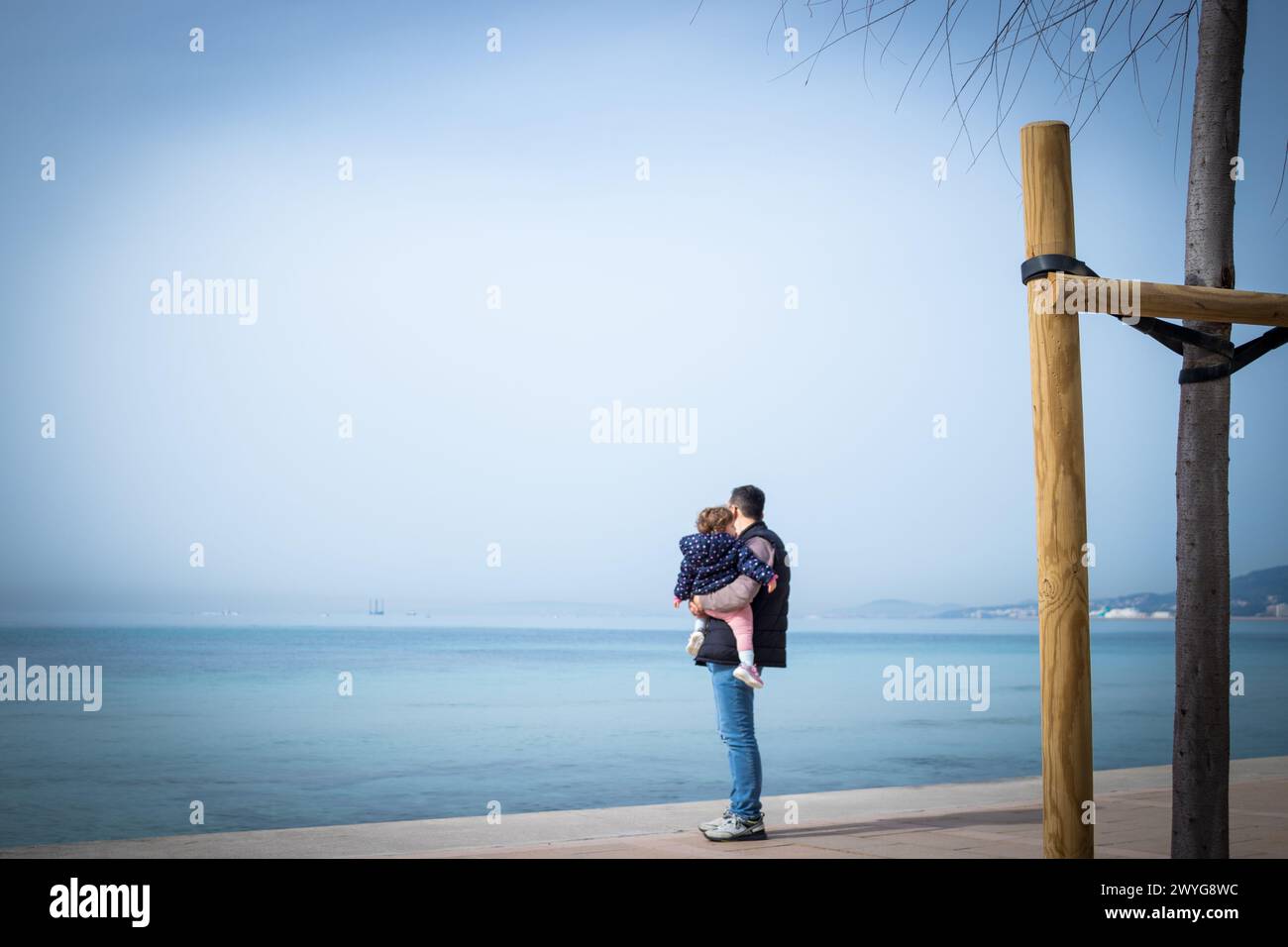 Ein ergreifendes Bild, in dem ein Vater und eine Tochter am Meer stehen, mit dem Rücken zur Kamera, während sie nachdenklich auf das Meer blicken. Der Vater ist so Stockfoto