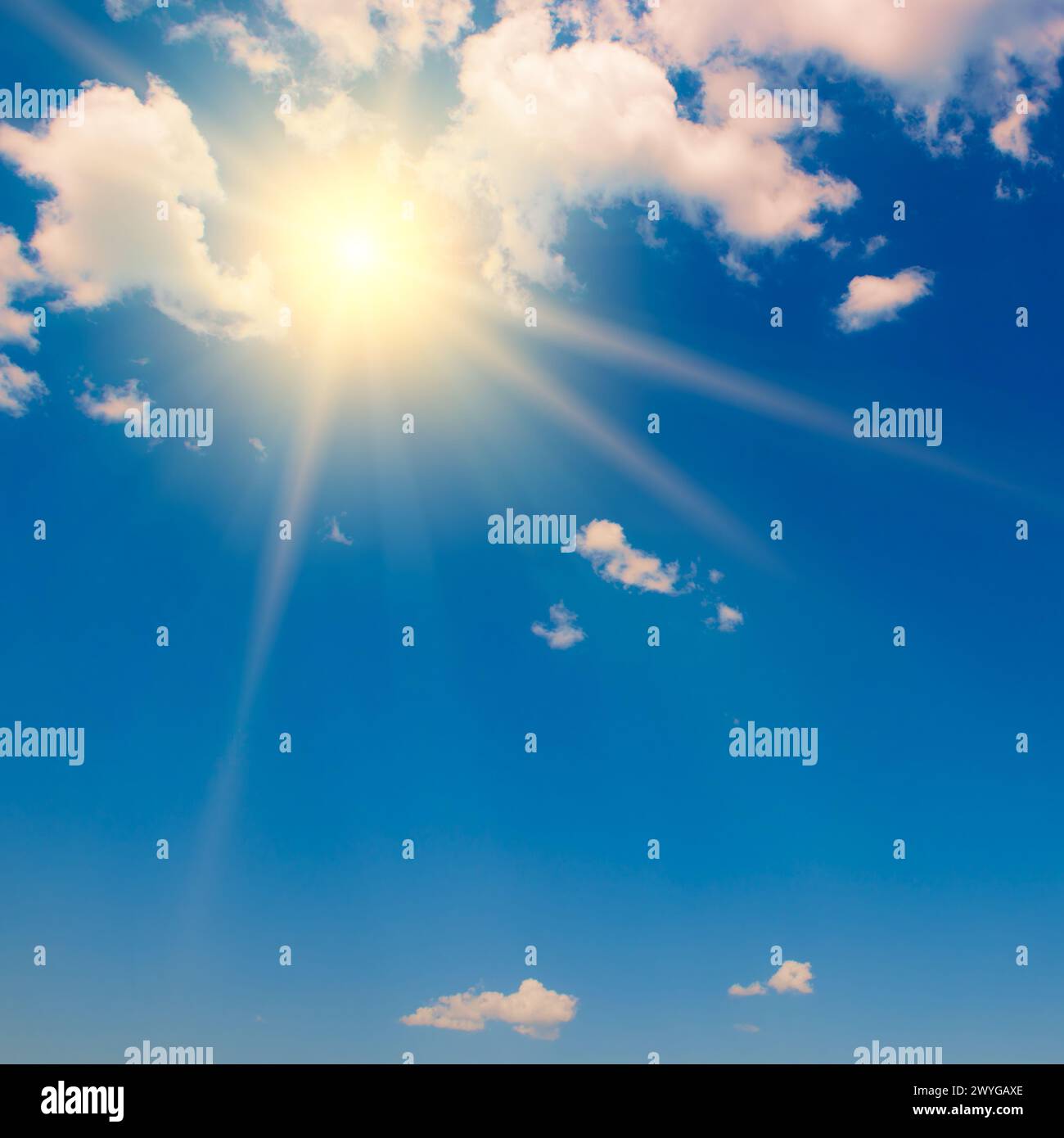 Blauer Himmel mit weißen, flauschigen Wolken und heller Sonne mit Strahlen. Stockfoto