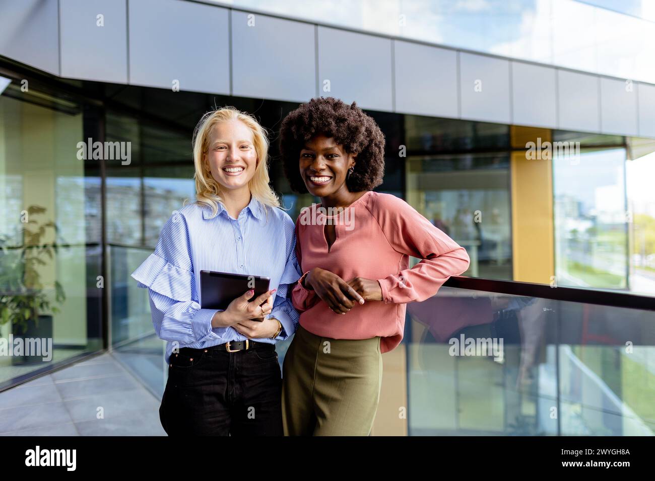 Zwei Frauen mit ähnlichen Merkmalen stehen nebeneinander, lächelnd, vor der großen Architektur. Stockfoto