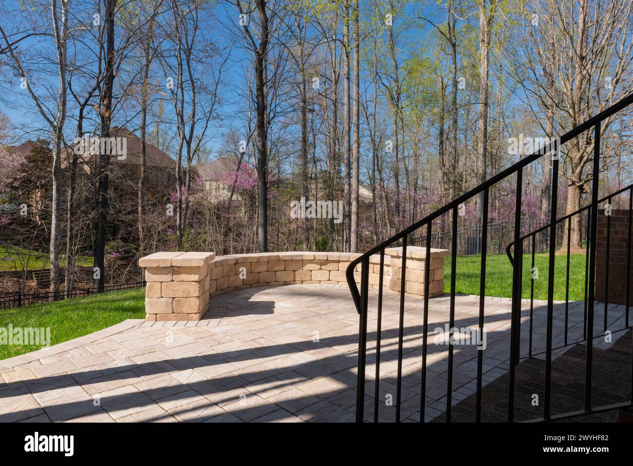 Malerischer Blick auf den Hinterhof im Frühling mit Terrassenpflastern und Steinmauer, blühenden weißen Kirschbäumen und frühlingshaften Hölzern im Hintergrund. Stockfoto