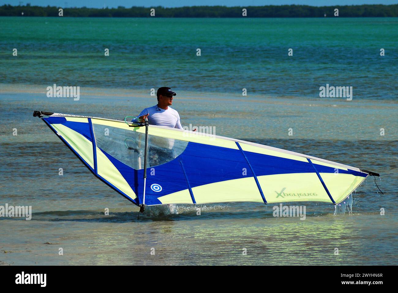 Ein erwachsener Mann beginnt nach einem Tag auf dem Wasser sein Windsurfbrett zu zerbrechen Stockfoto