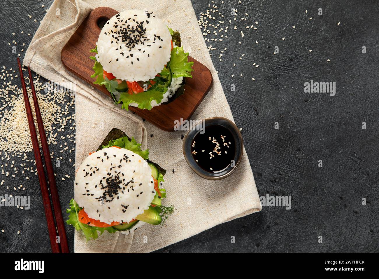 Asiatischer Sushi-Burger, Sojasauce, Essstäbchen auf dunklem Hintergrund. Trendiges Hybrid-Essen. Draufsicht, Kopierraum Stockfoto