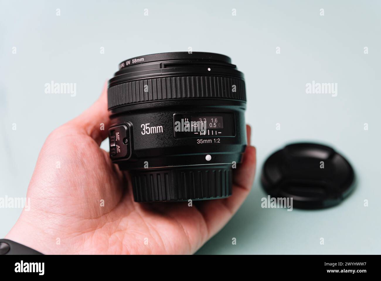 Nahaufnahme einer Hand, die ein 35-mm-DSLR-Kameraobjektiv mit einem UV-Filter hält, bereit für eine Fotosession vor einem weichen blaugrünen Hintergrund. Stockfoto
