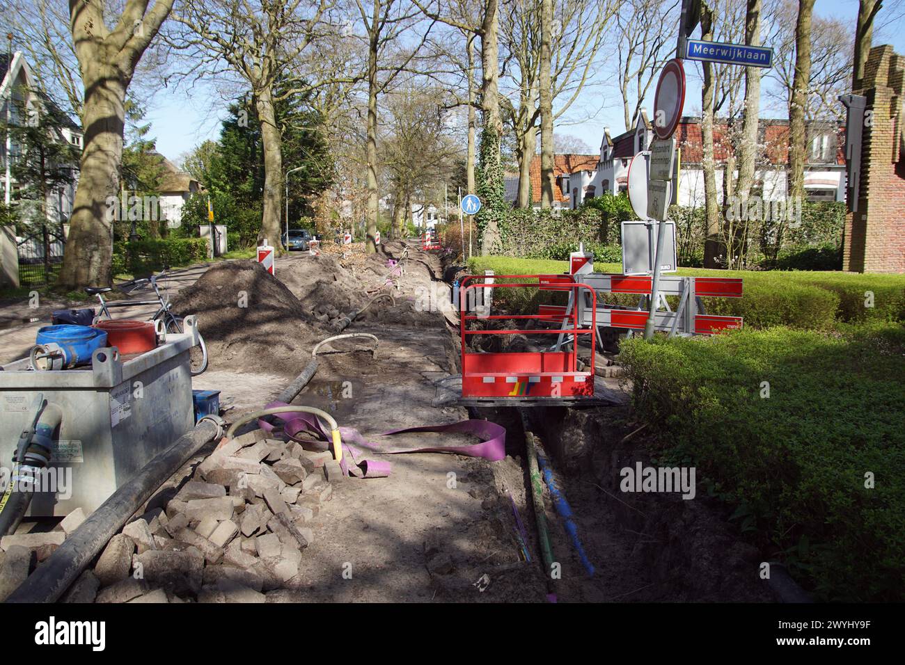 Straßenarbeiten in der Straße mit einem Loch, Pflastersteinen, Strom-, Gas- und Telekommunikationskabeln und Wasserleitungen. Straßenschilder. Sluislaan. Stockfoto