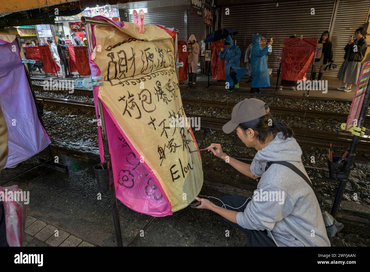 Der junge Mann malt sorgfältig Kalligraphie auf eine große Himmelslaterne, um sich das chinesische Neujahr zu wünschen Stockfoto