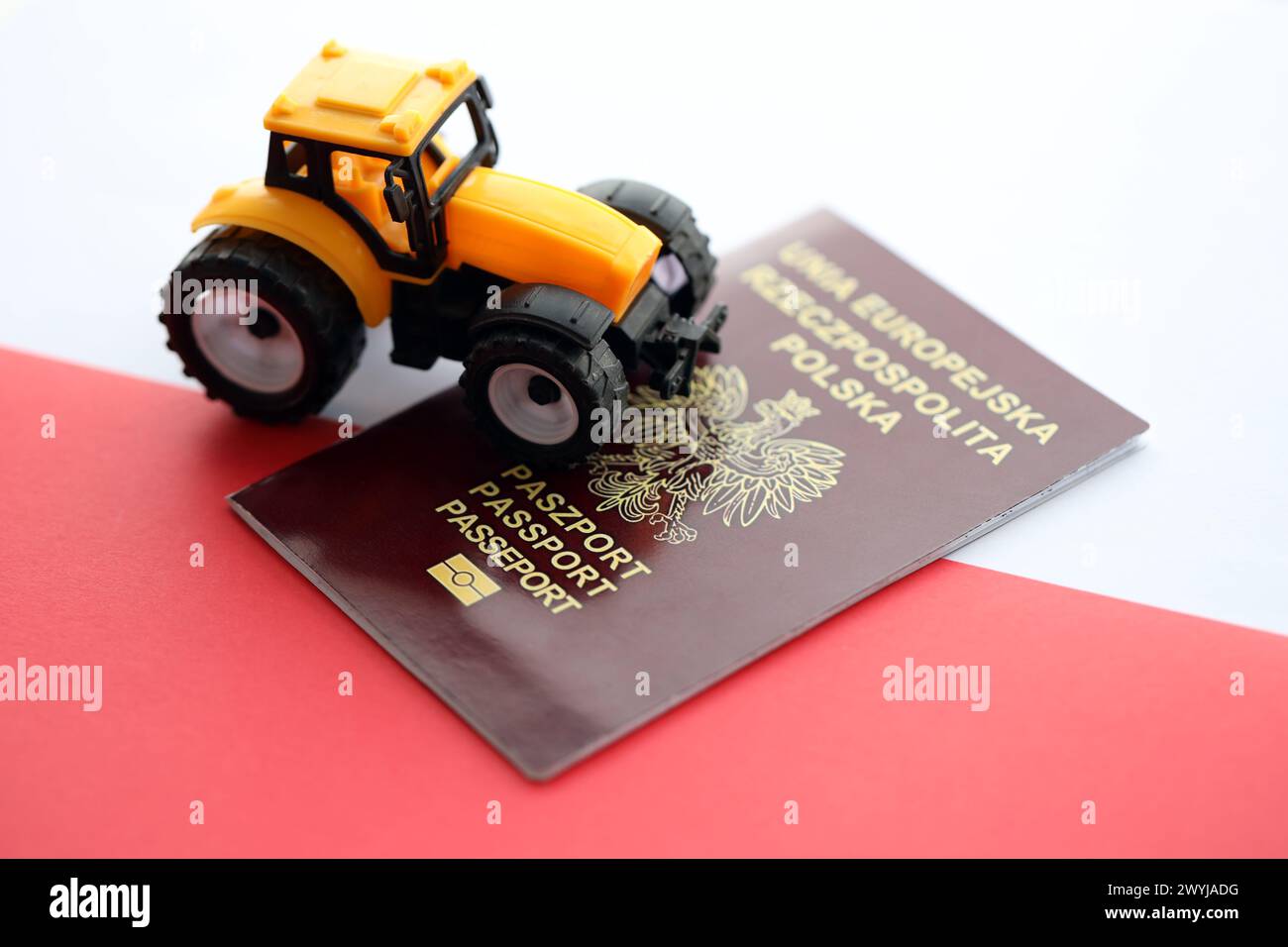 Roter polnischer Pass und gelber Traktor auf glatter rot-weißer Flagge von Polen Nahaufnahme Stockfoto