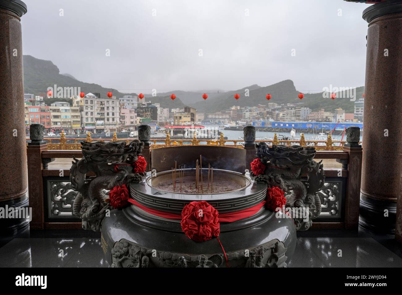 Ruhiger Blick auf einen Hafen von einem Tempelbalkon mit roten Laternen und brennendem Weihrauch vor nebeliger Kulisse Stockfoto