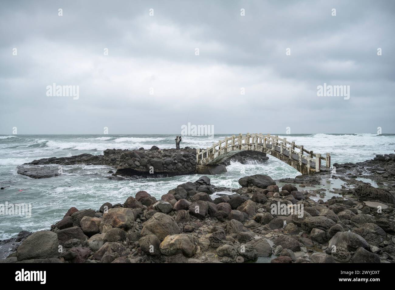 Fischer, die an einem bewölkten Tag von einem Felsvorsprung ins Meer angeln Stockfoto