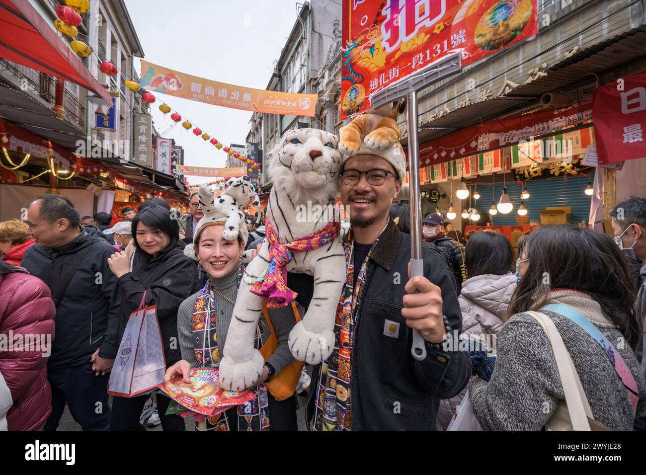 Ein glückliches Paar posiert mit Plüschtigerspielzeug während einer festlichen Veranstaltung in einer geschmückten Straße während des chinesischen Neujahrs. Stockfoto