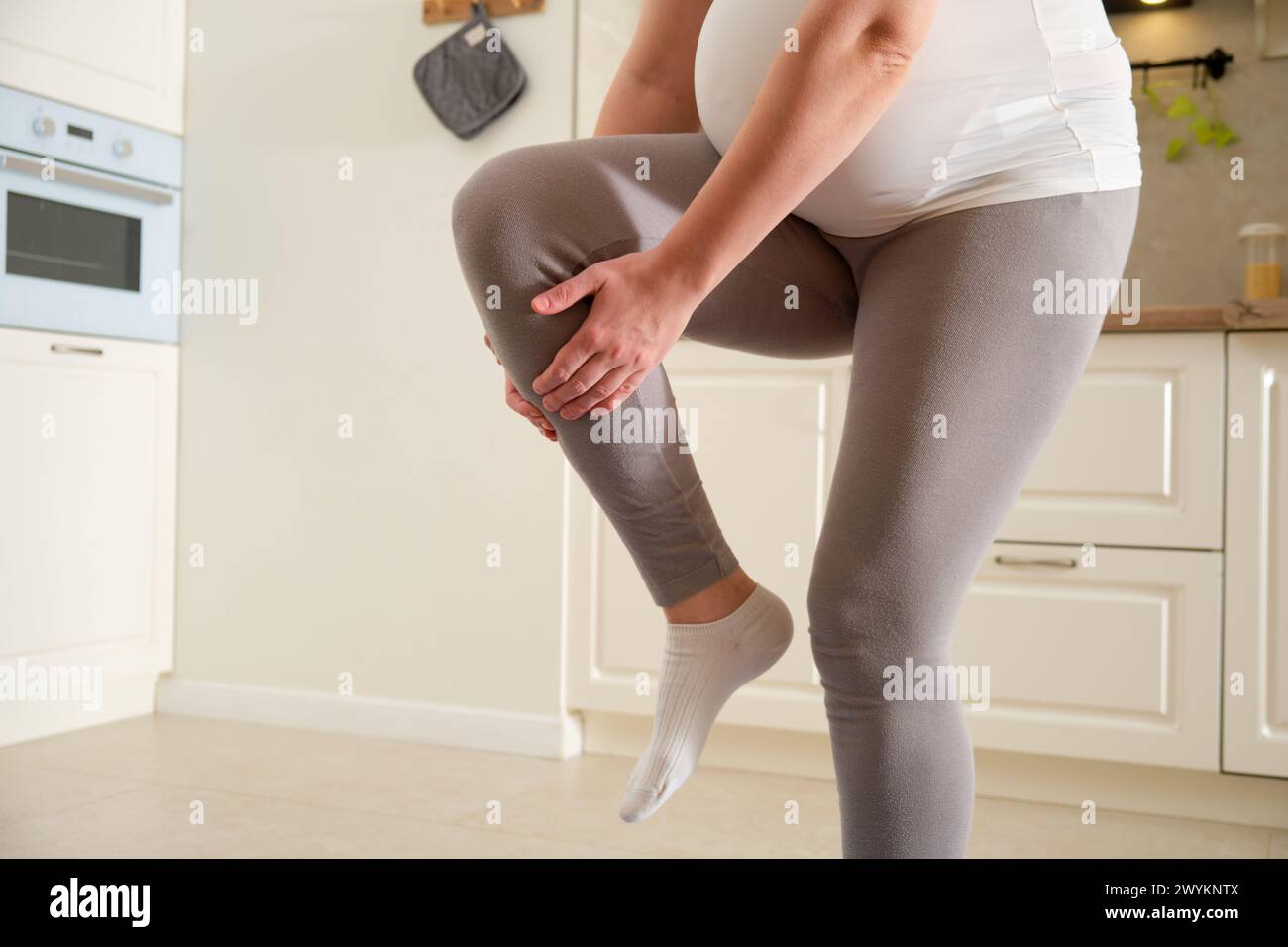 Fitness zu Hause während der Schwangerschaft und Probleme bei einer Beinverletzung. Schwangere Frau beim Sporttraining hält sich an einem gekrümmten Knie fest Stockfoto