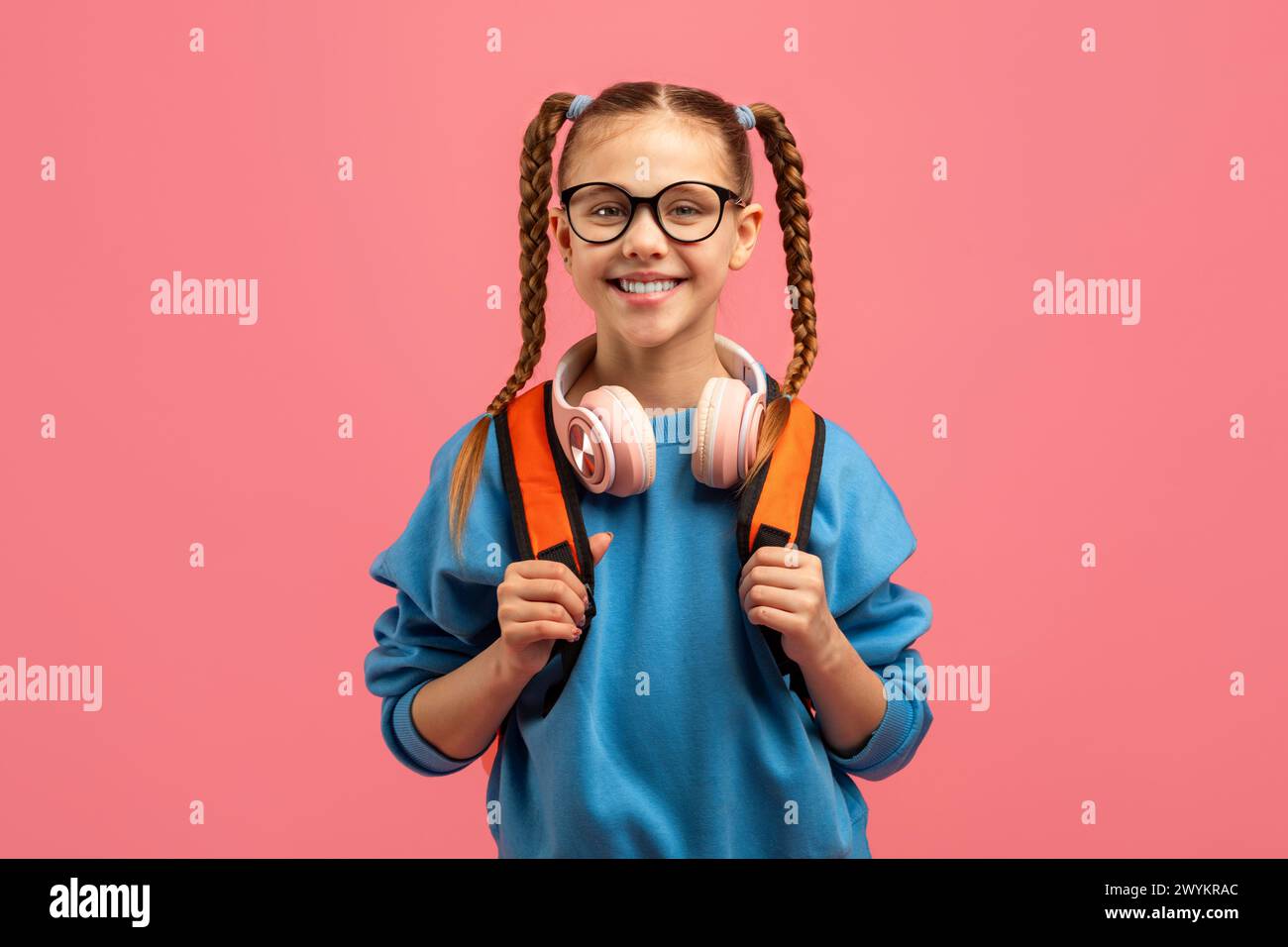 Lächelndes Mädchen mit Kopfhörern und Rucksack auf rosa Hintergrund Stockfoto
