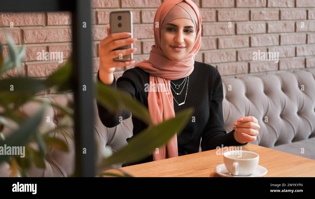 Selfie im Café. Online-Stream. Hübsche Frau im Hijab macht Fotos und erstellt Inhalte für Blog-Internetgespräche in einem gemütlichen Café. Stockfoto