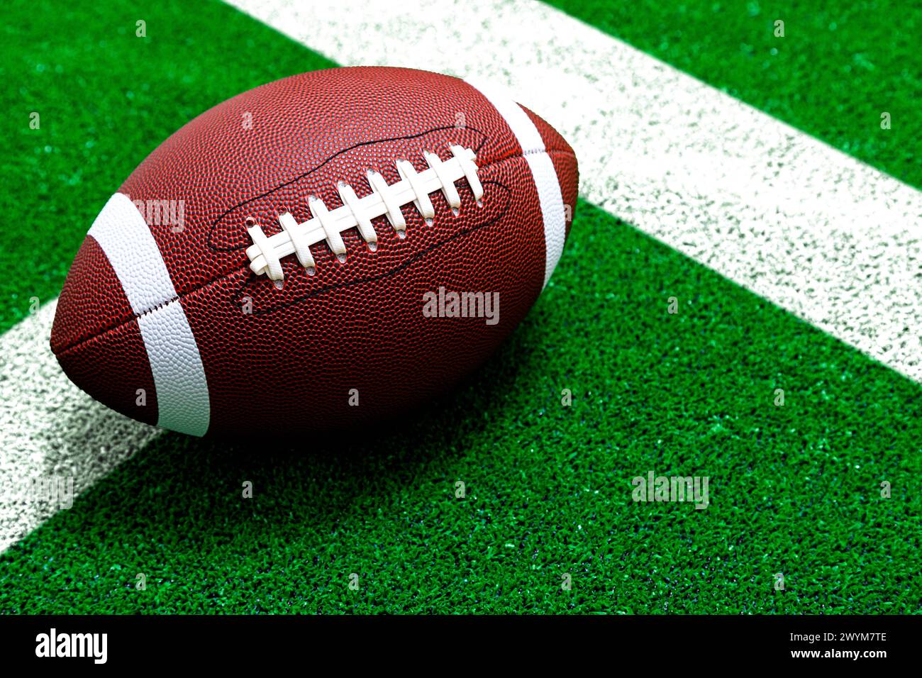 Ein strukturierter American Football auf dem grünen Kunstrasen mit weißer Linie. Stockfoto