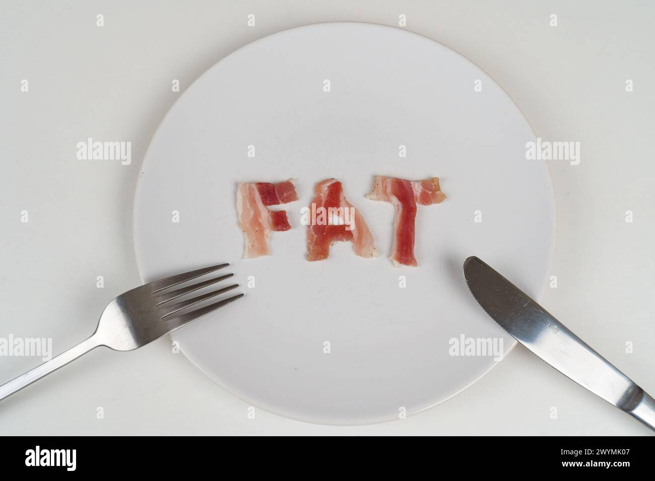 Ein Teller mit dem Wort Fett darauf, begleitet von einer Gabel und einem Messer, symbolisiert ungesunde Essgewohnheiten. Stockfoto