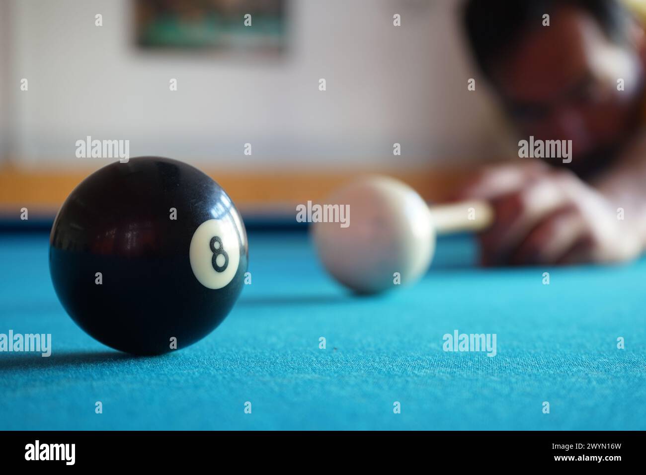 Mann, der den weißen Ball auf die schwarze Nummer 8 und das Loch auf einem blauen Snookertisch trifft. Stockfoto