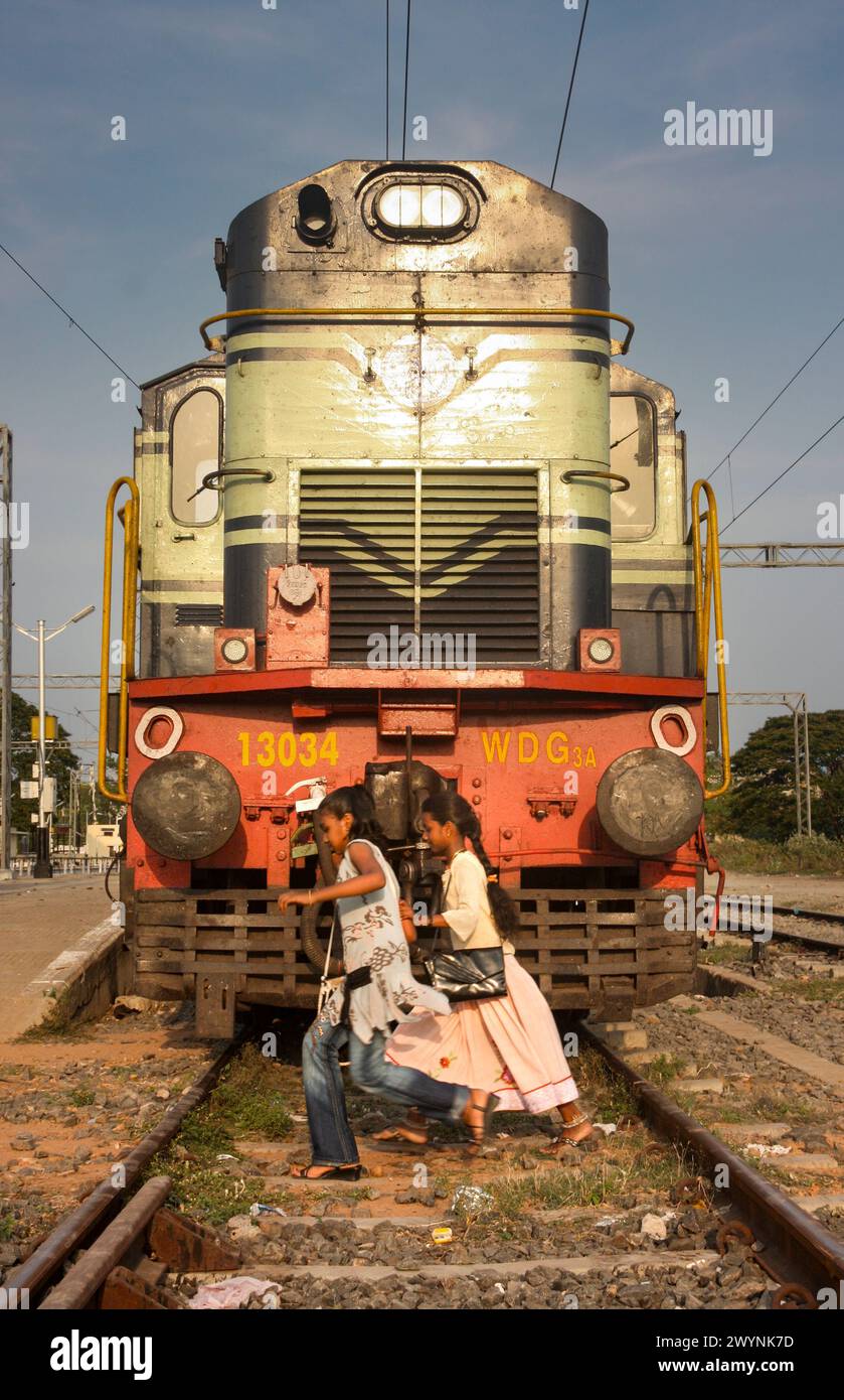 Kinder, die über die Eisenbahnlinie vor der Lokomotive am Bahnhof Puducherry (Pondicherry) in Indien fahren Stockfoto