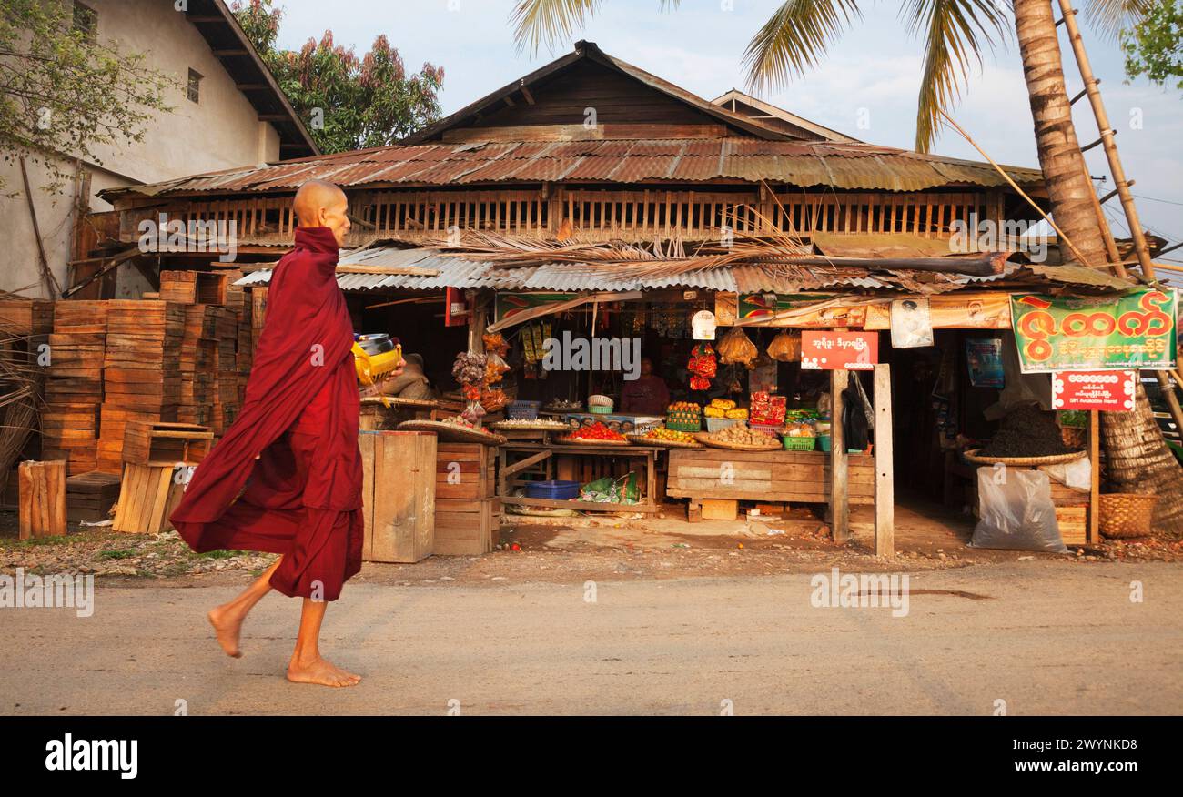 Buddhistischer Mönch in purpurrotem Gewand sammelt Almosen aus dem Laden in Hsipaw, Myanmar Stockfoto