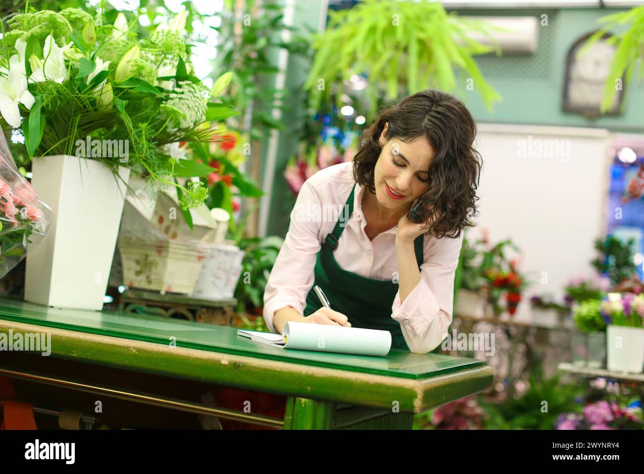 Florist im Blumengeschäft, der eine Bestellung von einem Kunden am Telefon entgegennimmt. Stockfoto