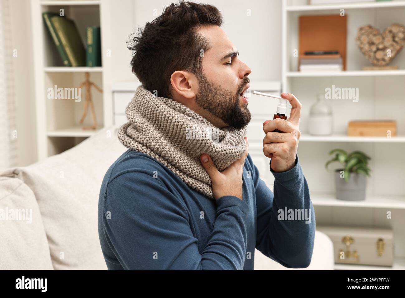 Junger Mann mit Schal mit Kehlspray in Innenräumen Stockfoto