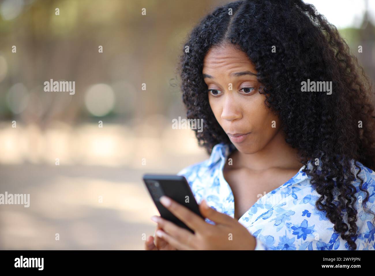 Eine verblüffte schwarze Frau, die draußen im Freien den Inhalt des Telefons überprüft Stockfoto