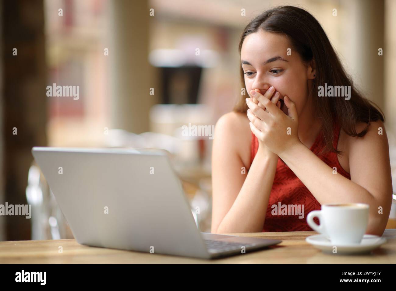Staunte Frau, die auf einer Restaurantterrasse Laptop-Inhalte überprüft Stockfoto