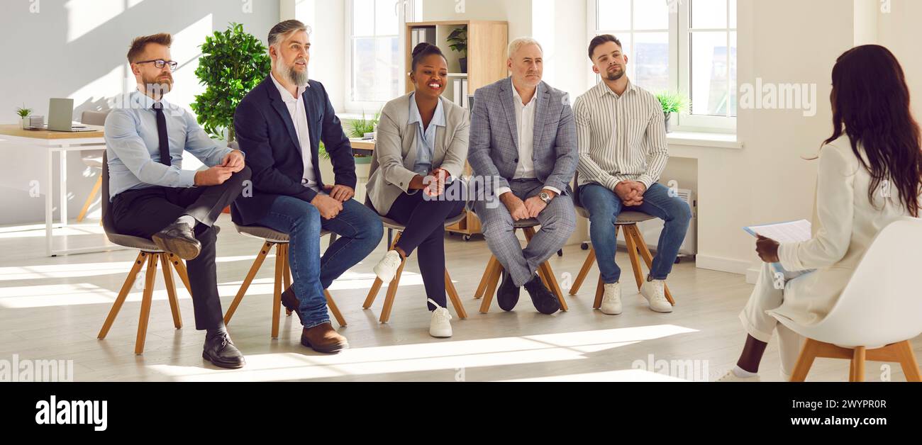 Ein Team aus verschiedenen Unternehmensmitarbeitern sitzt im Büro und hört dem Business Coach zu Stockfoto