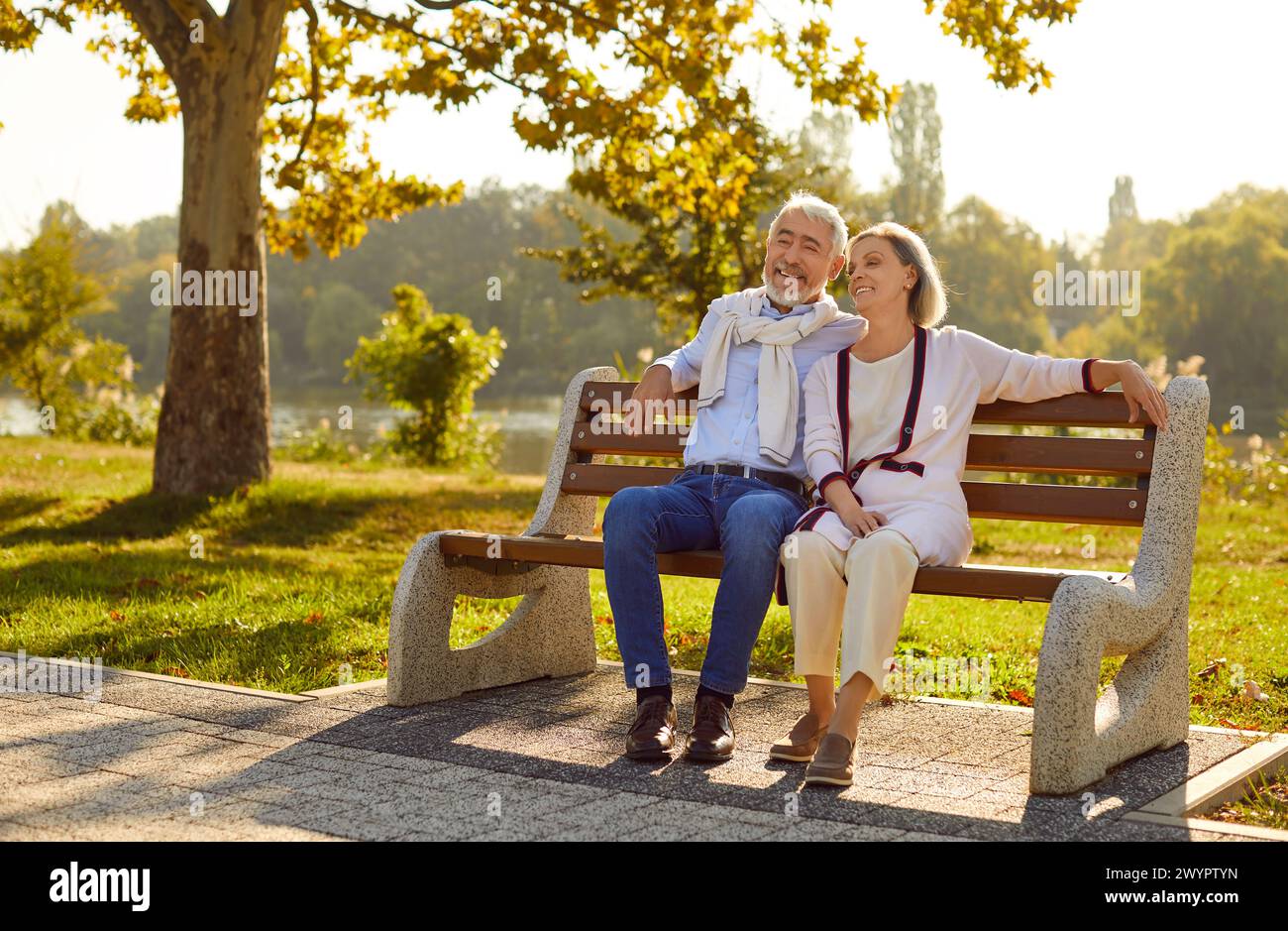 Ein wunderschönes, stilvolles älteres verliebtes Paar sitzt am warmen Sommerabend auf einer Bank im Stadtpark. Stockfoto