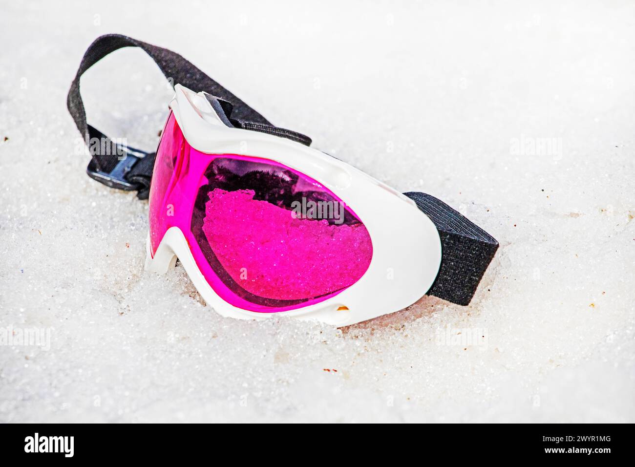 Die pinkfarbene Liegemaske liegt an einem sonnigen Tag auf einem nassen, schneebedeckten Hang. Winterschneesaison. Aktivurlaub mit Familie Stockfoto