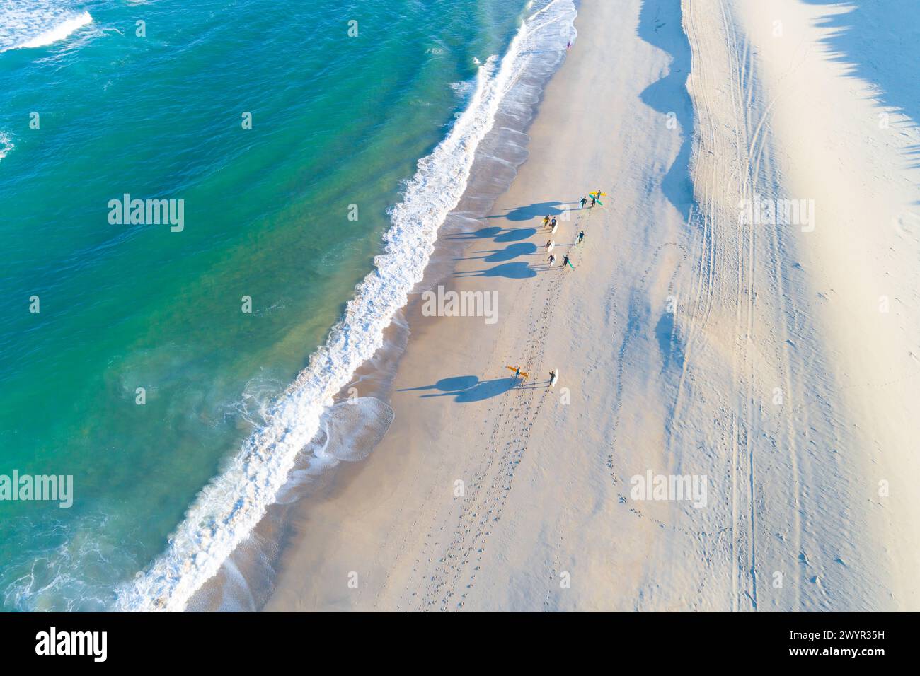 Eine Gruppe von Surfern, die mit ihren Surfbrettern am Ufer eines Strandes entlang laufen, aus der Vogelperspektive mit einer Drohne. Stockfoto