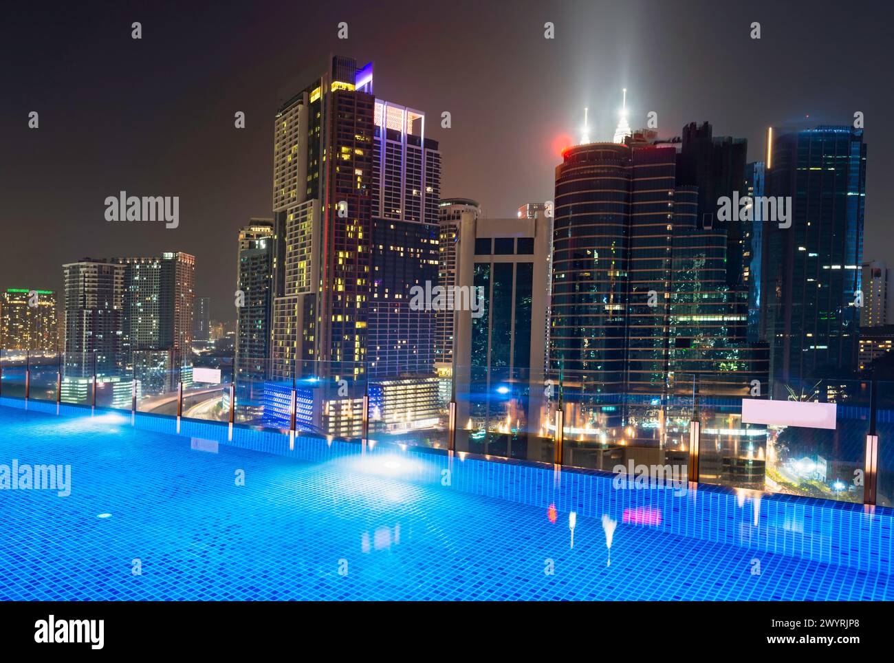 Atemberaubender Blick auf die Wolkenkratzer der Stadt KL, nachts hell beleuchtet, eleganter Pool im Vordergrund mit atemberaubendem Panoramablick Stockfoto
