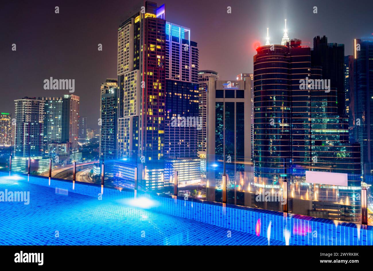 Atemberaubender Blick auf die Wolkenkratzer der Stadt KL, nachts hell beleuchtet, eleganter Pool im Vordergrund mit atemberaubendem Panoramablick Stockfoto