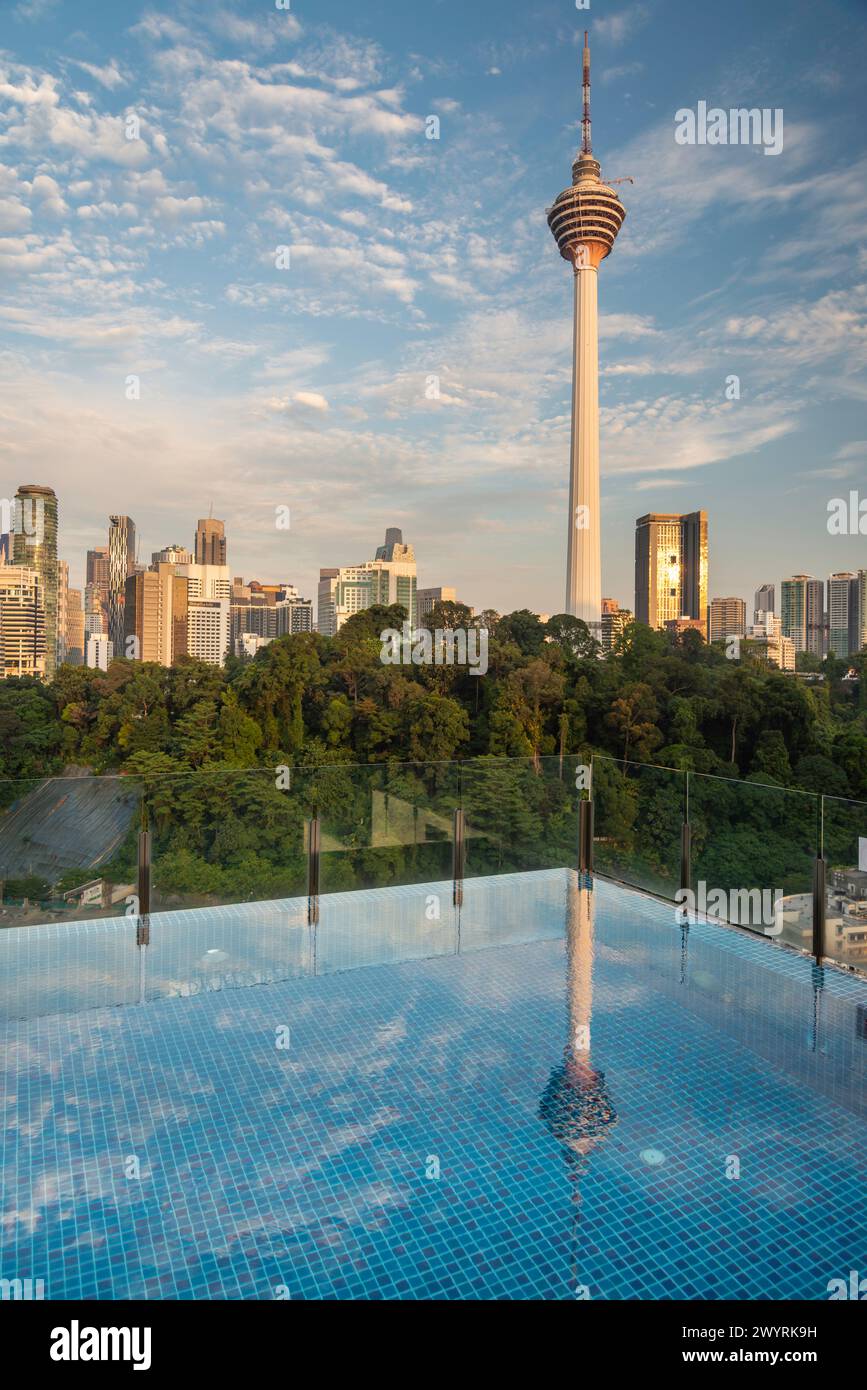 Atemberaubender Blick auf KL City und Menara Kuala Lumpur, in der Nähe des Sonnenuntergangs, mit blauem Infinity Pool auf der Dachterrasse im Vordergrund und blauem Himmel gesäumt Stockfoto