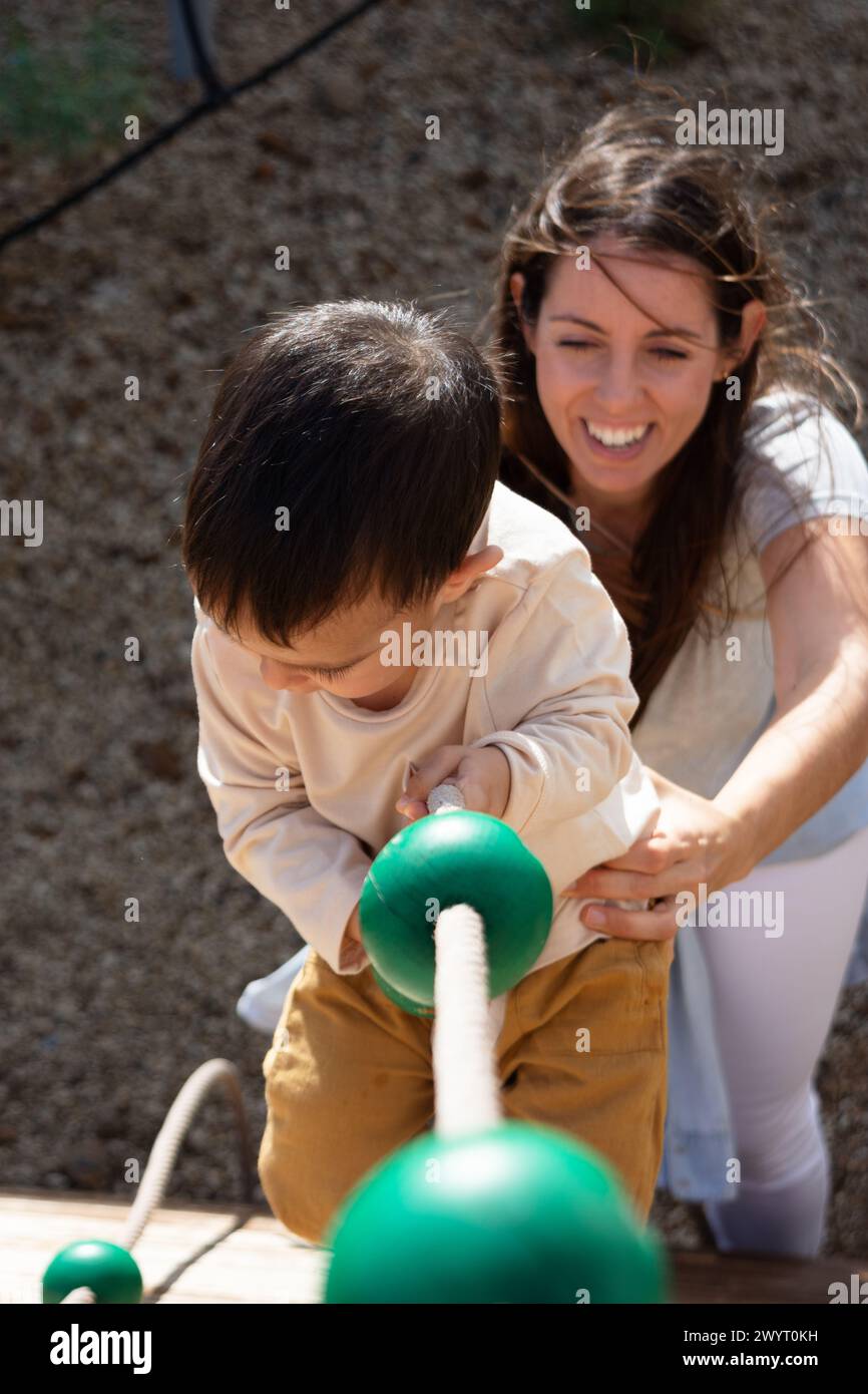 Baby klettert im Park mit ihrer Mutter an einem Seil Stockfoto