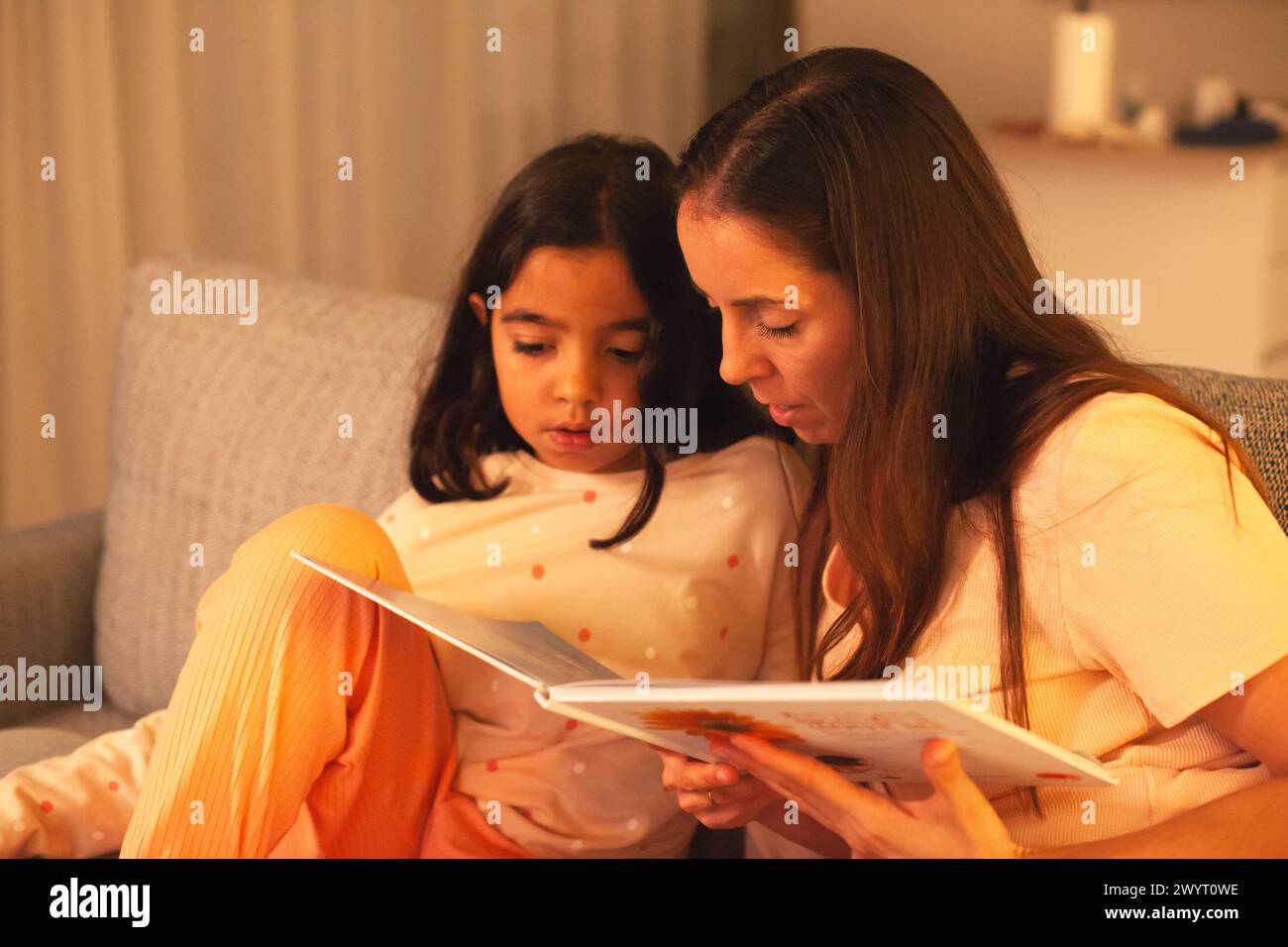 Mom und Tochter lesen vor dem Schlafengehen ein Buch auf der Couch Stockfoto