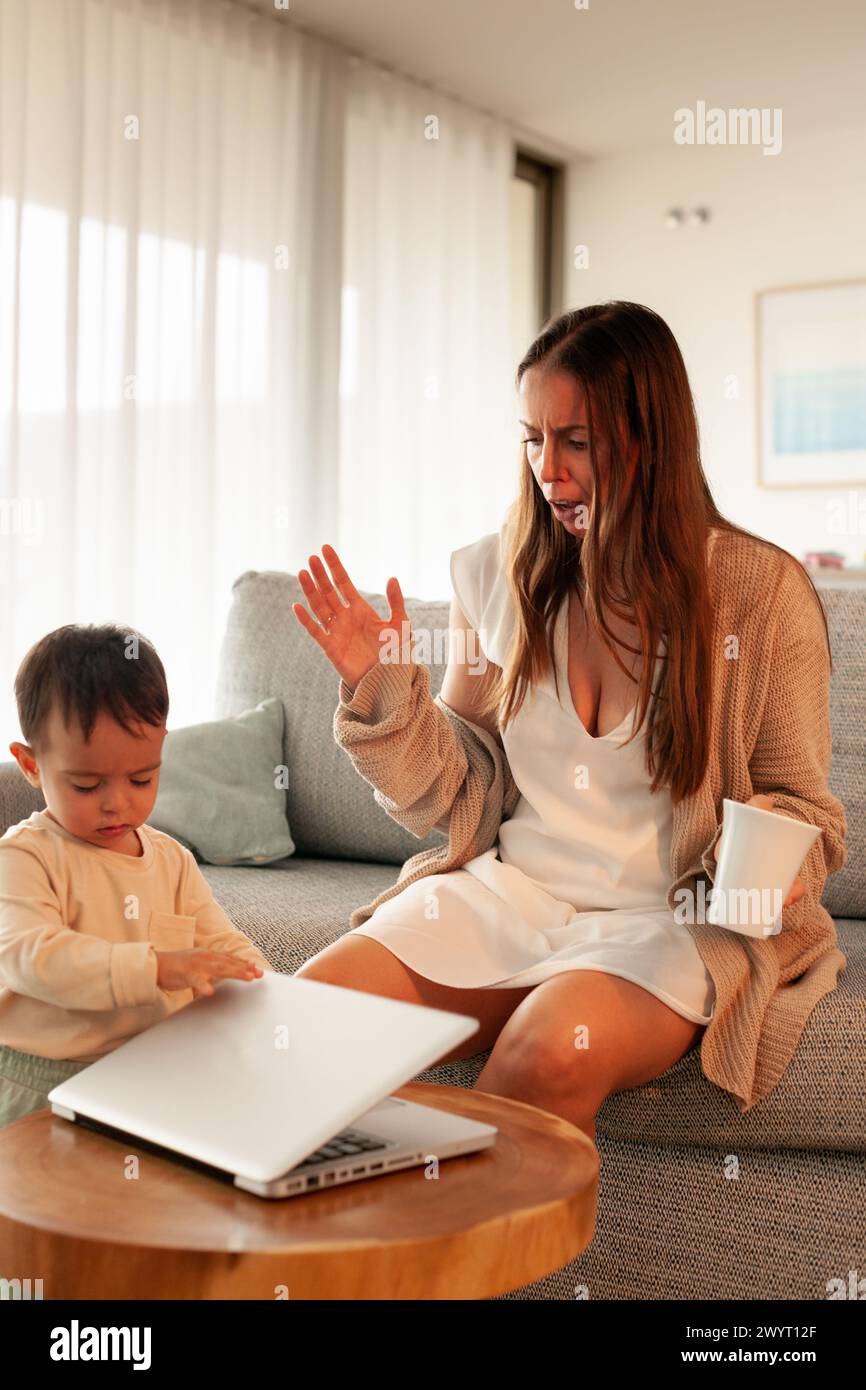 Mom ist sauer, weil ihr Baby ihren Laptop herunterfährt, als sie arbeitete Stockfoto