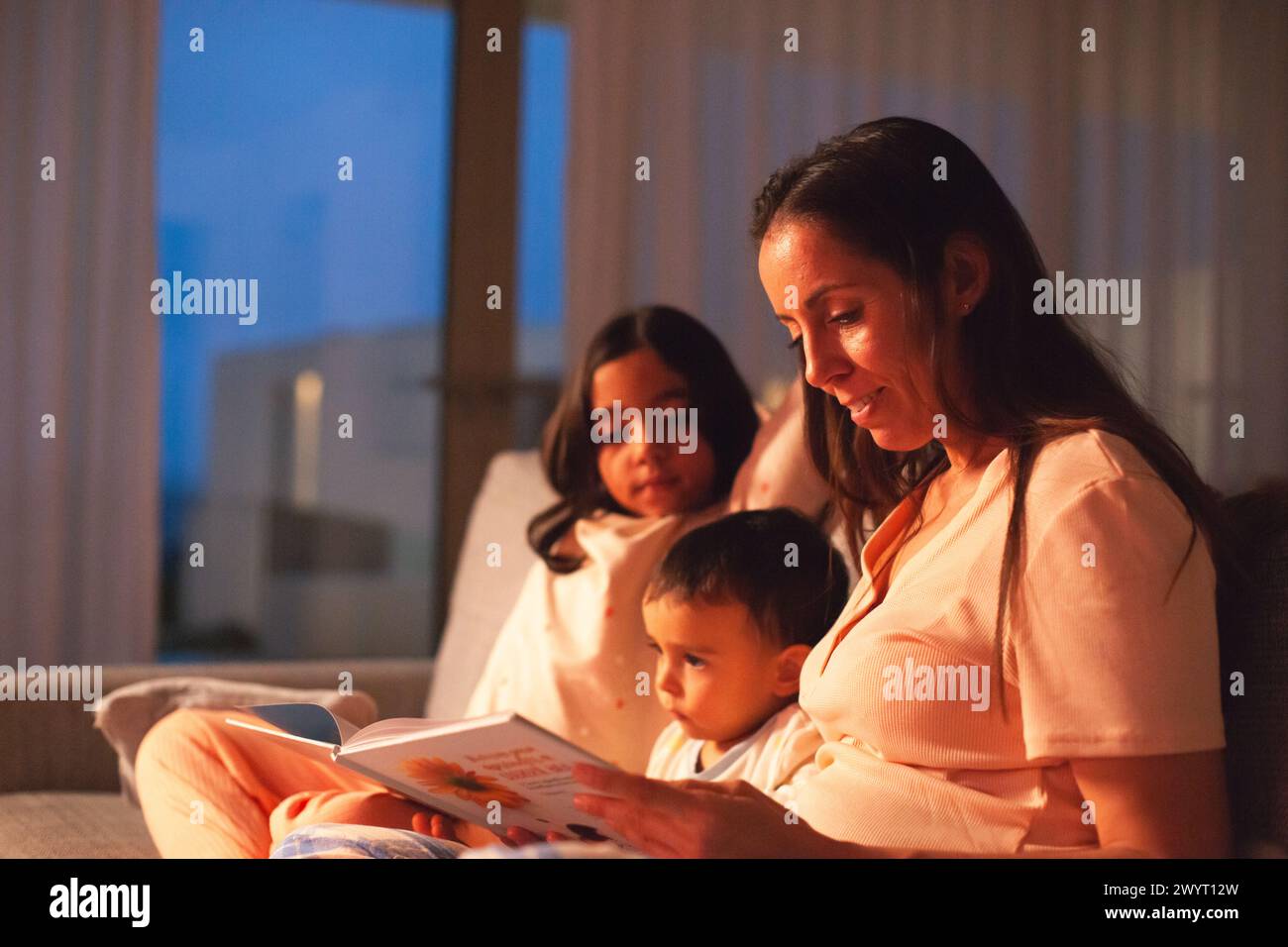 Mutter erzählt ihren Kindern eine Geschichte, wenn es dunkel wird Stockfoto