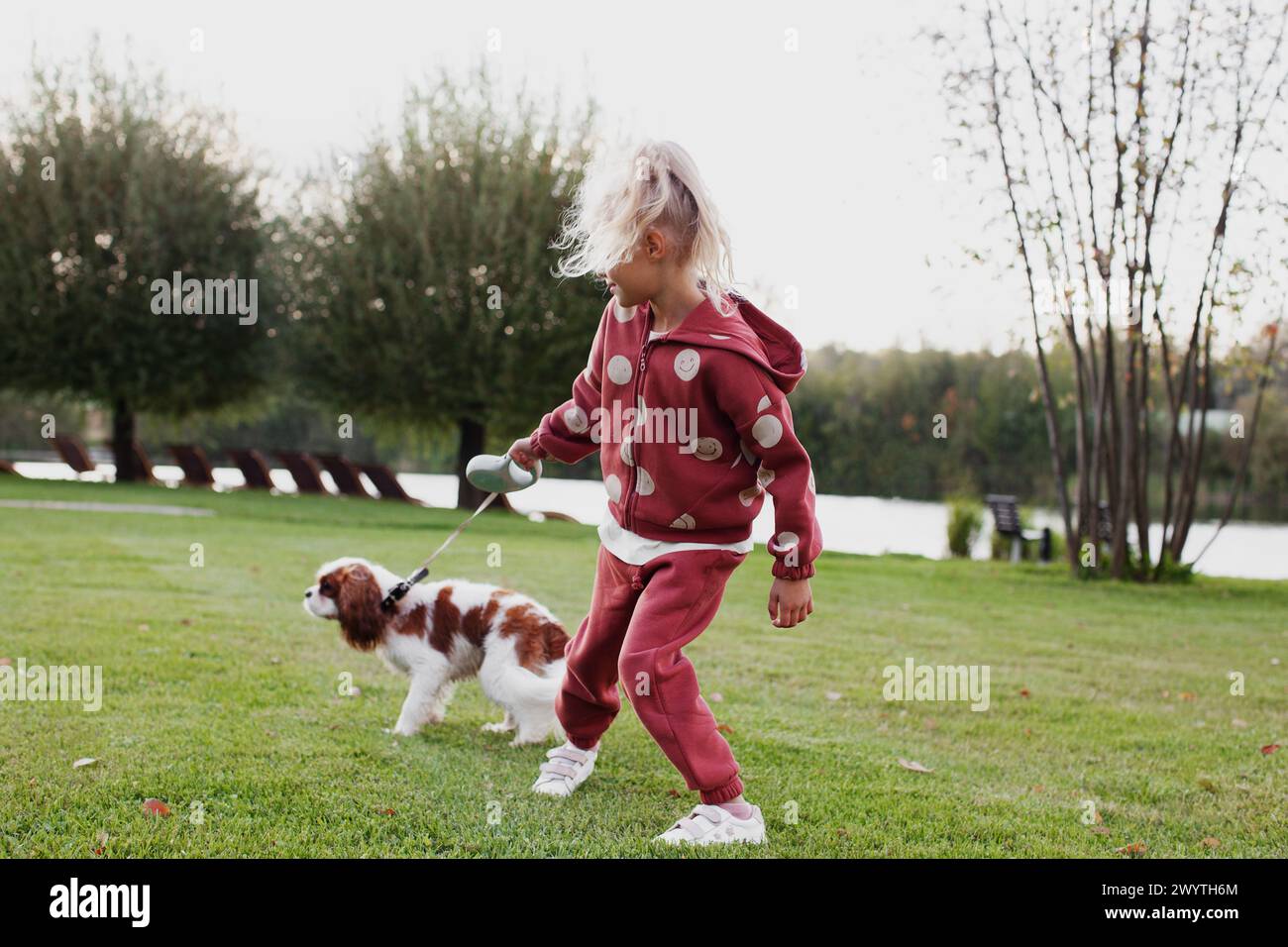 Blondes Mädchen, das draußen mit dem verspielten Spaniel-Haustier läuft und spielt. Glückliches Kind mit Hund in Bewegung. Stockfoto